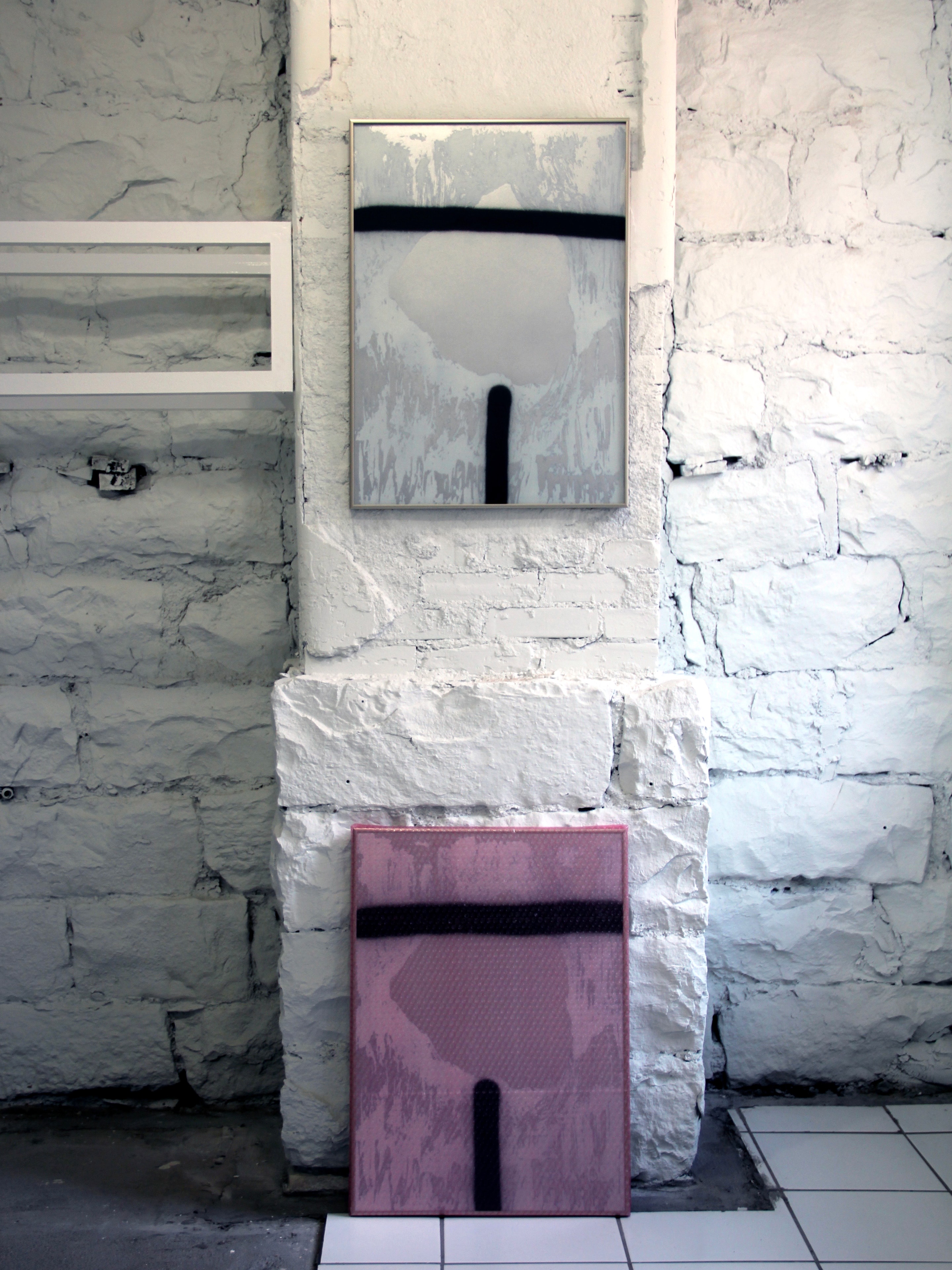 Two framed abstract artworks installed on a white-painted brick wall