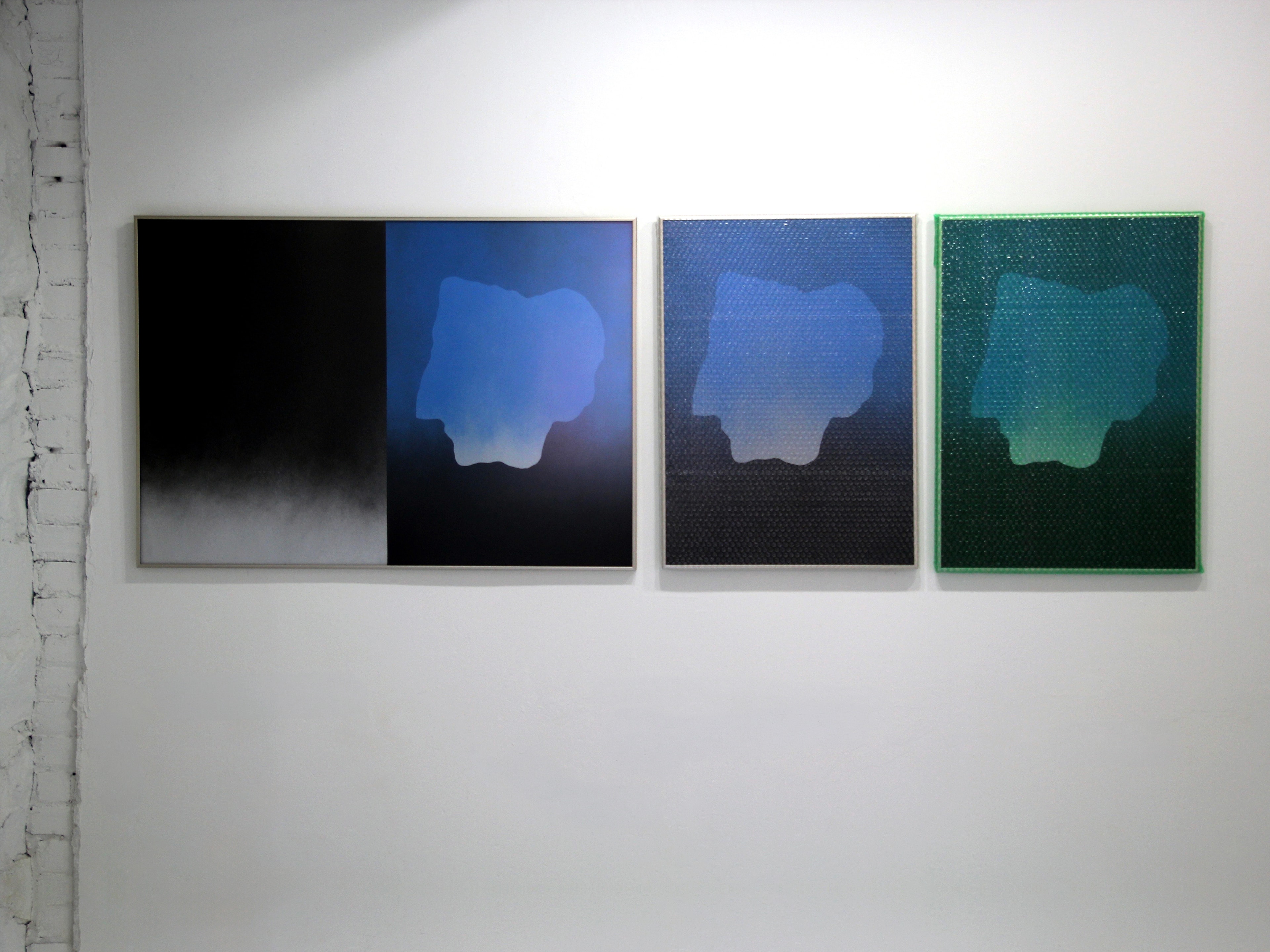 Three abstract artworks in blue, black, and green displayed on a white gallery wall