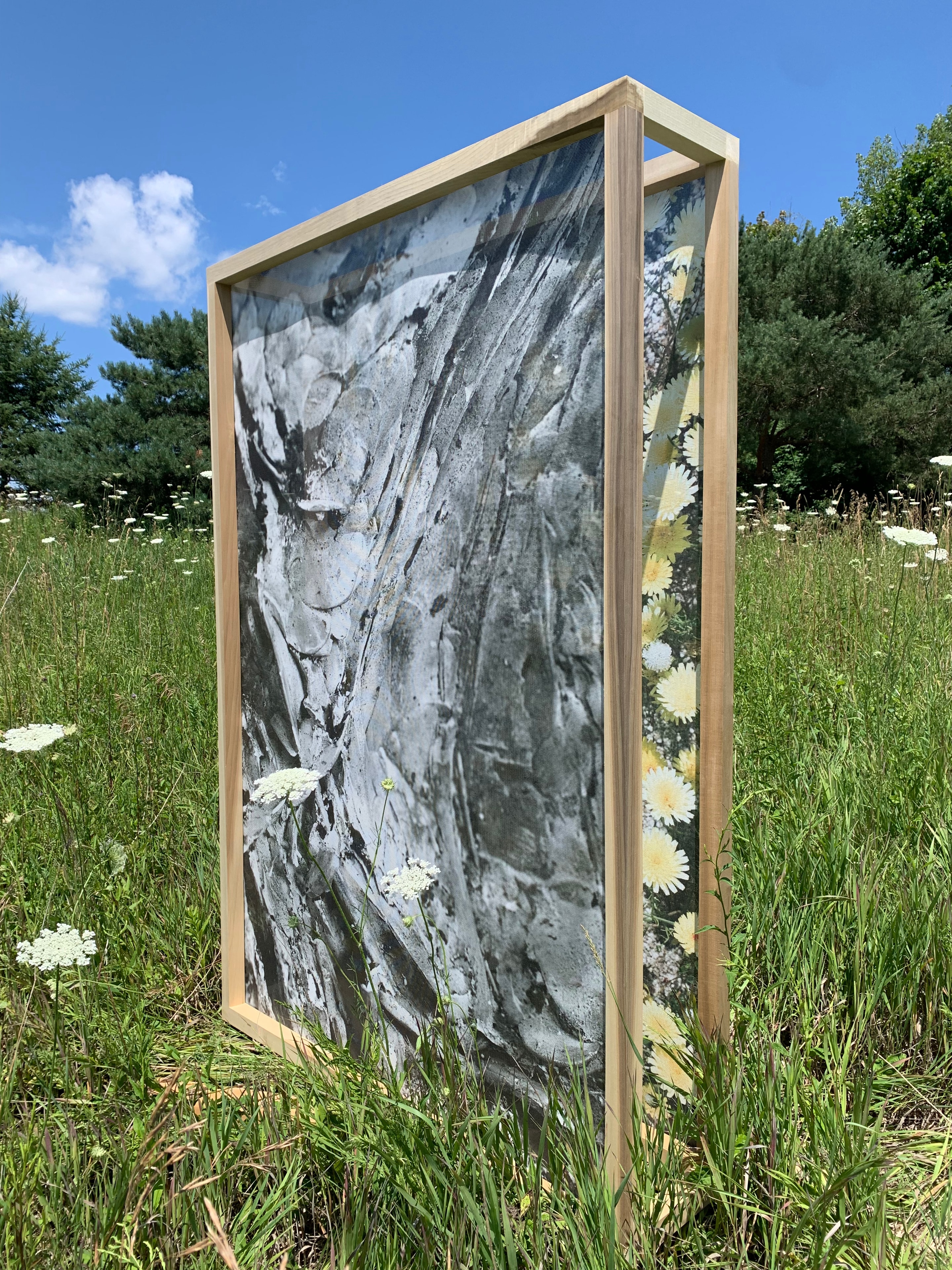Framed abstract artwork installed outdoors among grasses and wildflowers