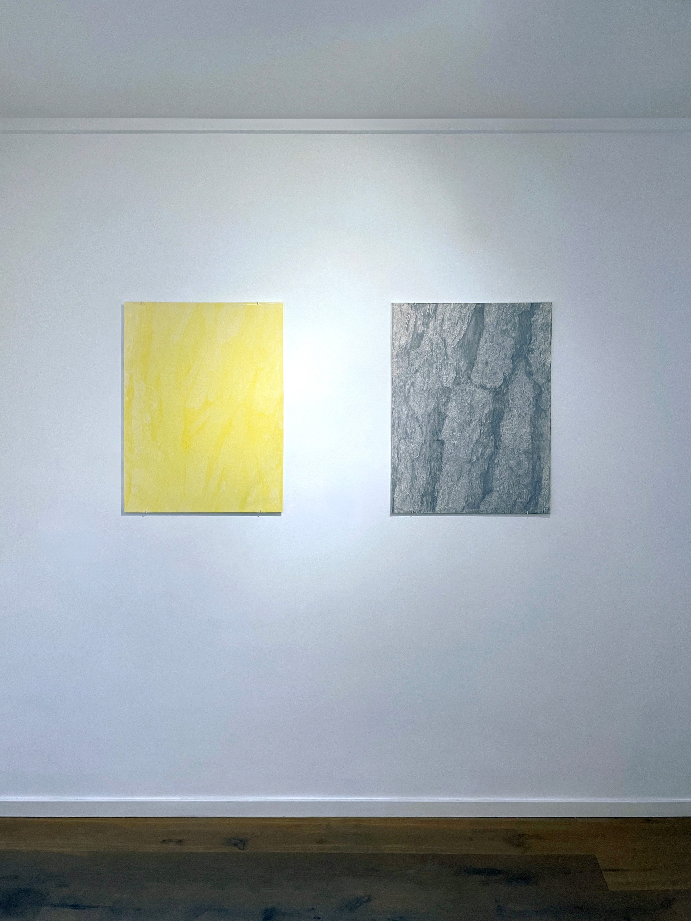 Two abstract transfer drawings, one yellow and one dark gray, installed on a white gallery wall